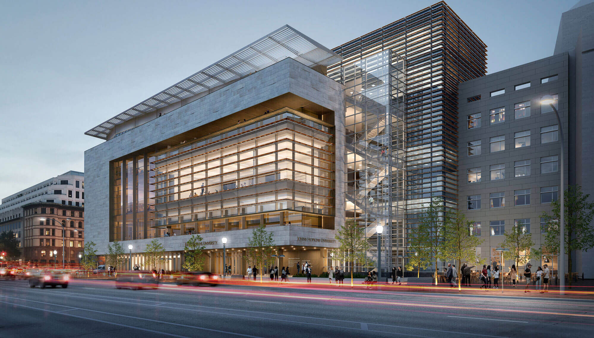 The Hopkins Bloomberg Center on Pennsylvania Avenue, with its stone facade, glass entrance and horizontal sunshades illuminated at dusk.