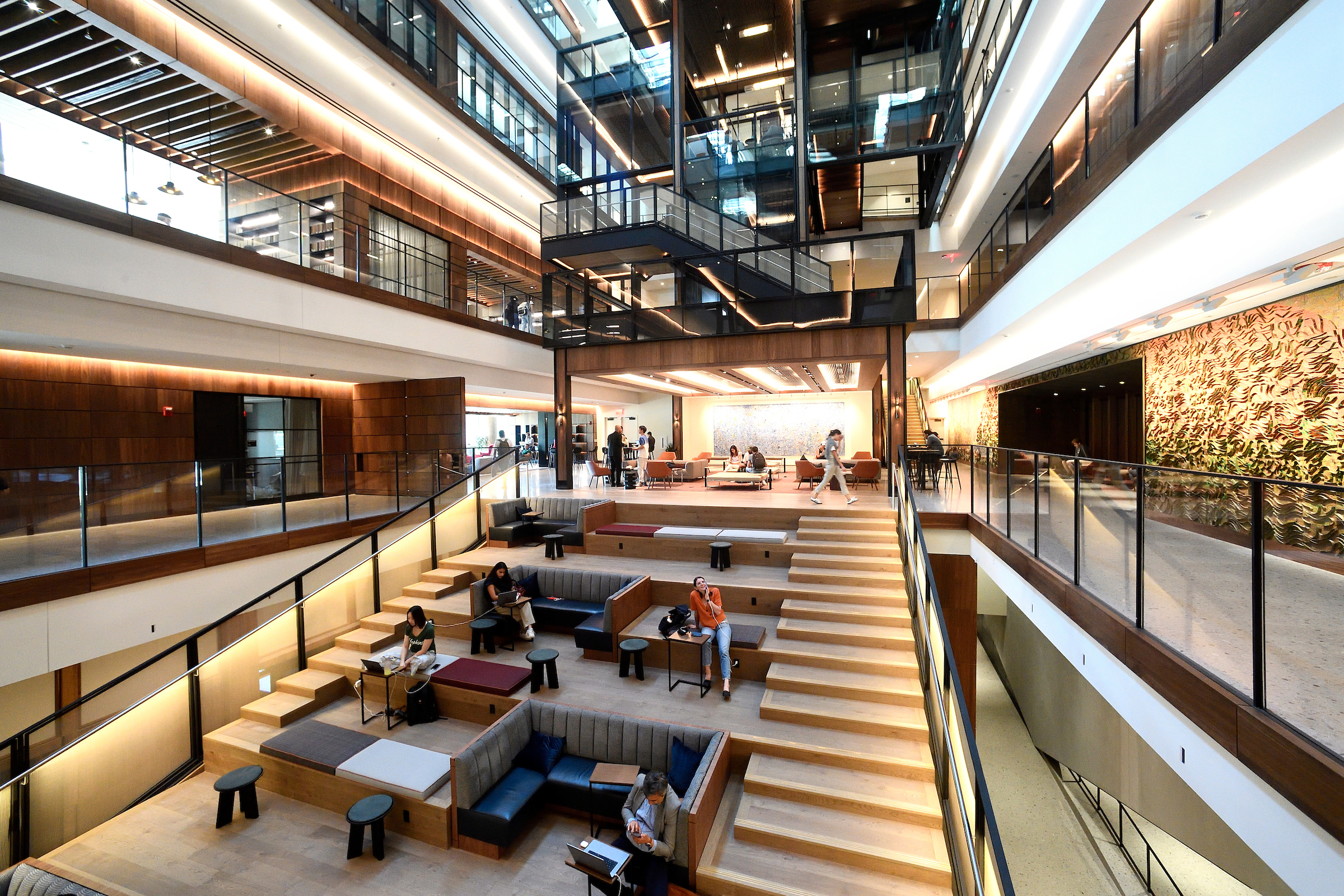 The Bloomberg Center’s real atrium, featuring tiered seating, warm wood finishes and suspended glass-enclosed stairs.